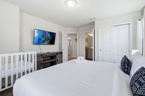 Une chambre d’hôtel avec un grand lit, un téléviseur fixé au mur, un bureau avec une chaise et un berceau.