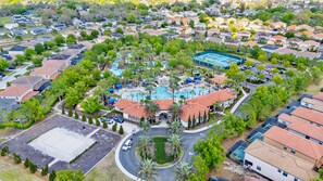 Vue aérienne d’un quartier résidentiel avec une piscine centrale entourée de maisons, un espace de stationnement et une allée circulaire aménagée.