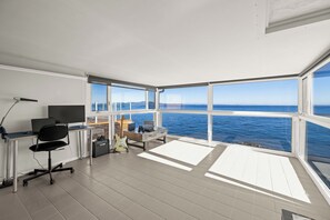 Une chambre moderne dotée d’une grande fenêtre donnant sur la mer, d’un bureau avec un ordinateur, d’une chaise et d’une guitare.