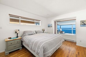 Une chambre à coucher avec un lit, une table de chevet, une lampe, une fenêtre donnant sur la mer et un tableau au mur.