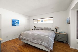 Une chambre à coucher avec un lit, des tables de chevet, une fenêtre et des œuvres d’art accrochées aux murs.