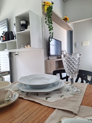 Et spiseområde med et bord dækket til to, en kaffemaskine og et fjernsyn i baggrunden.
