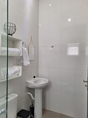 Et badeværelse med et hvidt pedestalvask, toilet og en brusekabine med glasvægge.