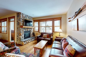 A cozy living room with a stone fireplace, leather sofas, and a television. - Tree Tops by Okanagan Premier (Beaverdell)