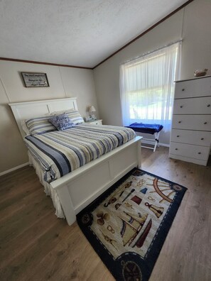 Une chambre à coucher comprenant un lit, une table de chevet, une commode, un meuble à tiroirs et une fenêtre avec des rideaux.