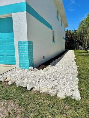 A building with a white exterior and a blue accent wall, a driveway with white gravel, and a grassy area with trees. - Bradenton Beach Escape | Steps from Beach&Trolley (Bradenton Beach)