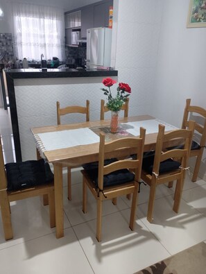 Ein Essbereich mit Holztisch und -stühlen, einer Vase mit roten Blumen und einer Küche im Hintergrund.