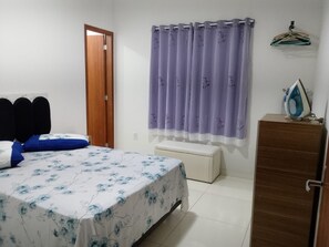 Ein Schlafzimmer mit Bett, Sitzbank, Kleiderschrank, Tür und Vorhang.