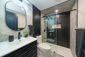 Et moderne badeværelse med et marmorbadevægsbord, en glasafskærmet brusekabine og et toilet.
