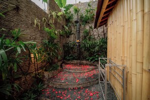 Un escalier en pierre, parsemé de pétales de fleurs rouges, entouré d’une végétation luxuriante et bordé de murs en bambou.