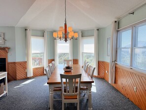 Ein Esszimmer mit einem langen Holztisch, weißen Stühlen, einer Kristallleuchtre und großen Fenstern mit Jalousien.