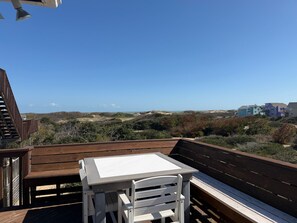 Eine Holzterrasse mit Tisch und Stühlen, mit Blick auf einen Strand und Dünen.