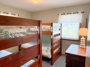 Ein Zimmer mit zwei Holzbettstapeln, einem kleinen Schreibtisch mit Lampe und einem Vorhangfenster.