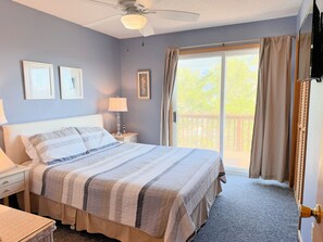 Ein Schlafzimmer mit Bett, Nachttischen, einer Lampe, einem Deckenventilator und Blick ins Freie durch eine Schiebetür.