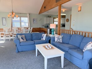 Ein Wohnzimmer mit blauem Sofa, einem weißen Couchtisch und einem Essbereich mit Holztisch und Stühlen.