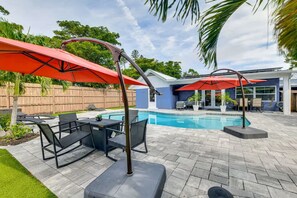 Una piscina con zona solarium, inclusi mobili da esterno e ombrelloni.