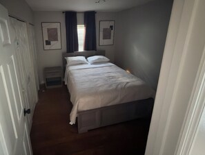 Un dormitori amb llit, una nitzeta, una finestra amb cortines i una porta.