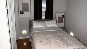 Un dormitorio con una cama, dos mesitas de noche, una ventana con persianas y una obra de arte en la pared.