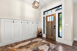 A hallway with a wooden door, a white wall with a built-in bench, and a hanging light fixture. - The Outlook: Modern, Private, Chef’s Kitchen (Wasilla)