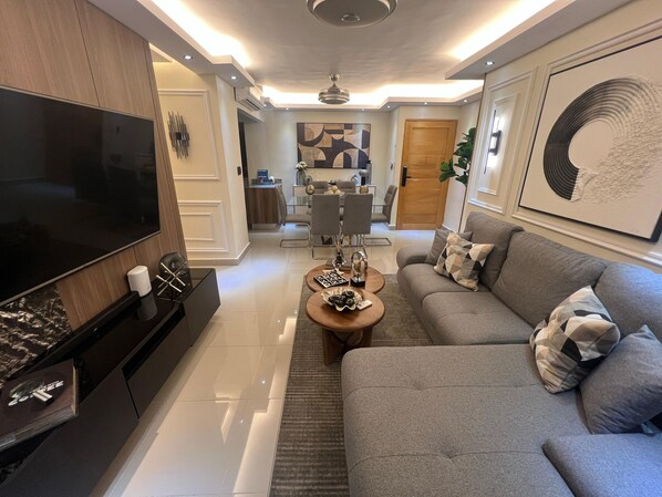 Ein modernes Wohnzimmer mit Fernseher, grauem Sofa und Couchtisch.