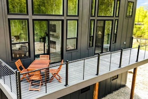 A modern building with large windows, a balcony with a railing, and outdoor seating.