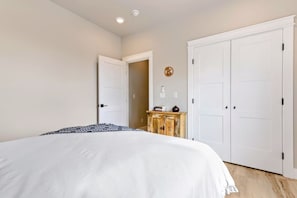 A bedroom with a large bed, two white doors, a wooden cabinet, and a wall-mounted clock.