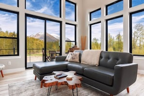 A modern living room with a sectional sofa, a wooden coffee table, and large windows offering a mountain view.