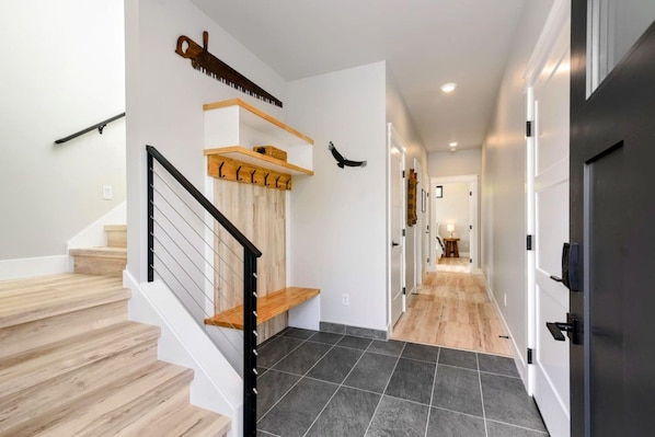 A modern interior with a staircase, wooden flooring, and a hallway leading to a door.
