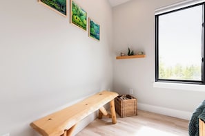 A room with a wooden bench, a window with a view of trees, and three framed pictures on the wall.