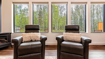 A room with two leather chairs facing a large window with a forest view.