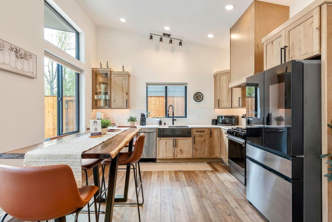 A modern kitchen with wooden cabinets, a stainless steel refrigerator, and a dining area with a table and chairs.