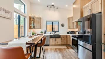 A modern kitchen with wooden cabinets, a stainless steel refrigerator, and a dining area with a table and chairs.