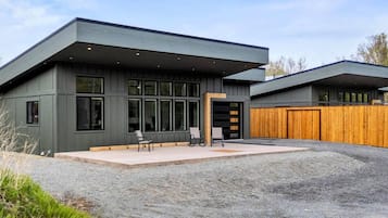A modern two-story building with a flat roof, large windows, and a covered outdoor seating area.