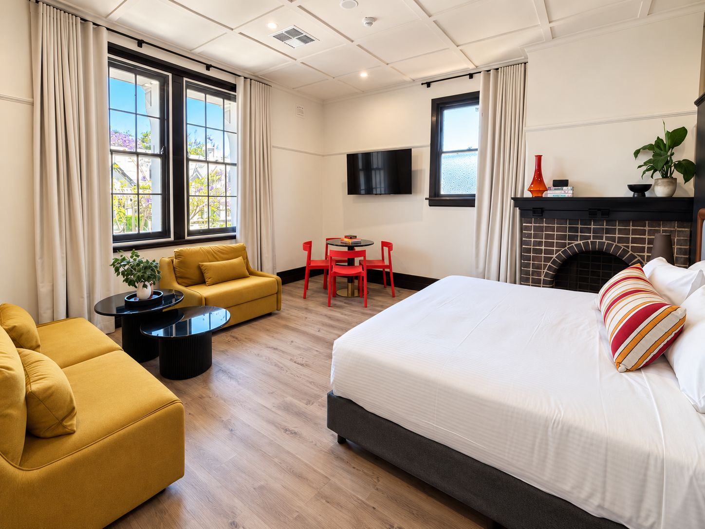 A hotel room with a bed, a sofa, a small table, a fireplace, and a TV.