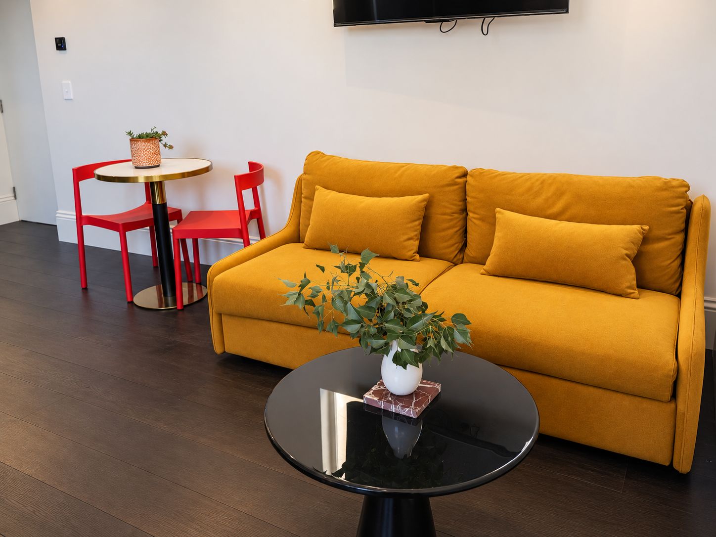 A modern living room with a sofa, a coffee table, a red chair, and a small round table with a plant.