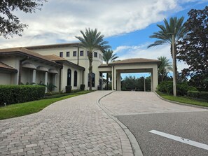 A building with a paved entrance, palm trees, and a clear sky.