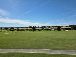 A golf course with a clear sky, a well-maintained green, and a row of houses in the background.