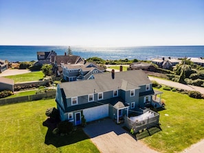 A two-story house with a garage, a fenced yard, and a view of the ocean. - Weekapaug's Largest Rental — 7 Bedrooms, Sleeps 14, Steps to Everything (Westerly)