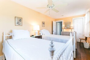 A hotel room with two beds, a ceiling fan, bedside lamps, a dresser, and a door leading to another room. - Weekapaug's Largest Rental — 7 Bedrooms, Sleeps 14, Steps to Everything (Westerly)