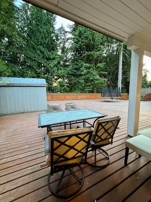 An outdoor patio with a table and chairs, surrounded by a wooden deck and a view of trees. - Spacious 3‑Bedroom Suite Near Grouse & Capilano-NV (North Vancouver)