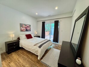 A bedroom with a bed, bedside tables, a nightstand, a painting, a sliding glass door, and a mirror. - Spacious 3‑Bedroom Suite Near Grouse & Capilano-NV (North Vancouver)