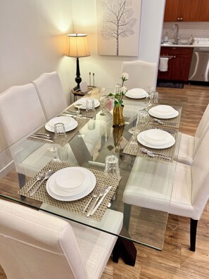 A dining table set with white plates, silverware, and clear glassware, surrounded by cushioned chairs. - Spacious 3‑Bedroom Suite Near Grouse & Capilano-NV (North Vancouver)