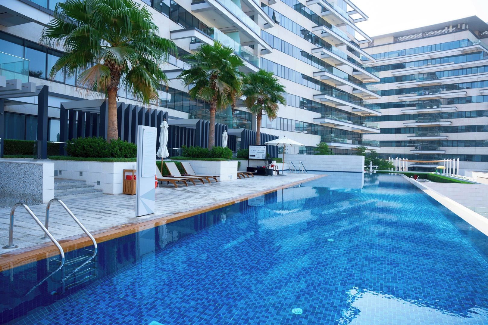 A modern hotel with a swimming pool, lounge chairs, and palm trees.