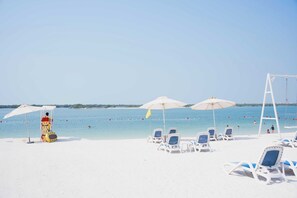 A beach with white sand, clear blue water, and several white umbrellas providing shade. - Luxury Jr. 1BR in Mayan Yas Island (Abu Dhabi)