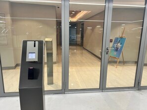 A modern interior with a glass door entrance, a digital payment kiosk, and a poster advertising swimming classes. - Luxury Jr. 1BR in Mayan Yas Island (Abu Dhabi)