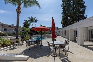Une terrasse extérieure avec des tables et des chaises, une piscine et des palmiers.