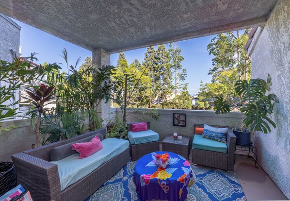 Une terrasse extérieure aménagée avec des meubles en osier, un tapis à motifs et des plantes en pot.