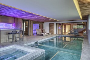 Un'area piscina moderna in interni con idromassaggio, poltrone relax e un angolo bar.
