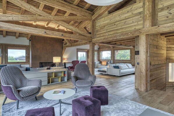 Un'ampia zona giorno con soffitto alto, travi in legno e grandi finestre che offrono vista sull'esterno.