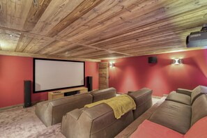 Une salle de cinéma privée dotée d’un grand écran, d’un plafond en bois, de murs rouges et de sièges en cuir.